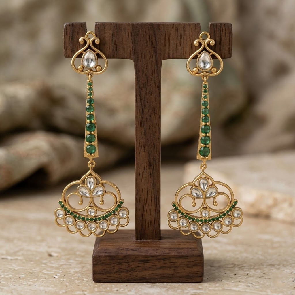 Ornate gold earrings with green and white stones on a wooden stand against a blurred natural background
