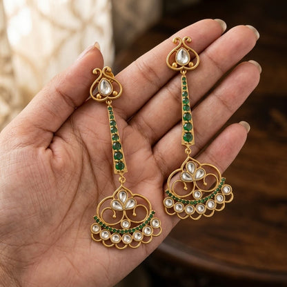 Gold earrings with green and white stones held in a hand against a blurred background