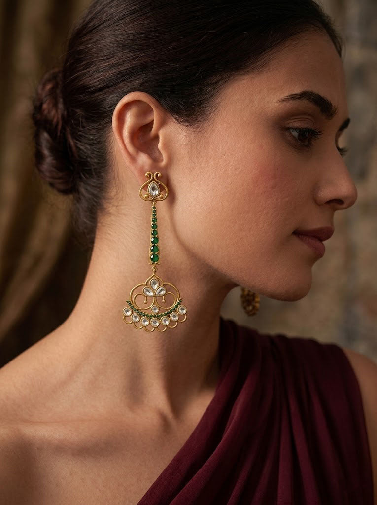 Woman wearing gold and green earrings with a blurred background