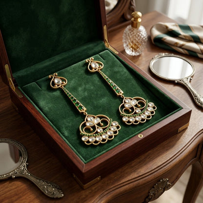 Ornate earrings in a green velvet box on a wooden table with mirrors and a handbag.