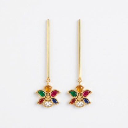 A pair of gold dangle earrings with long straight posts and a floral drop charm featuring multicolored enamel-like details and a clear central stone, shown on a plain white background.