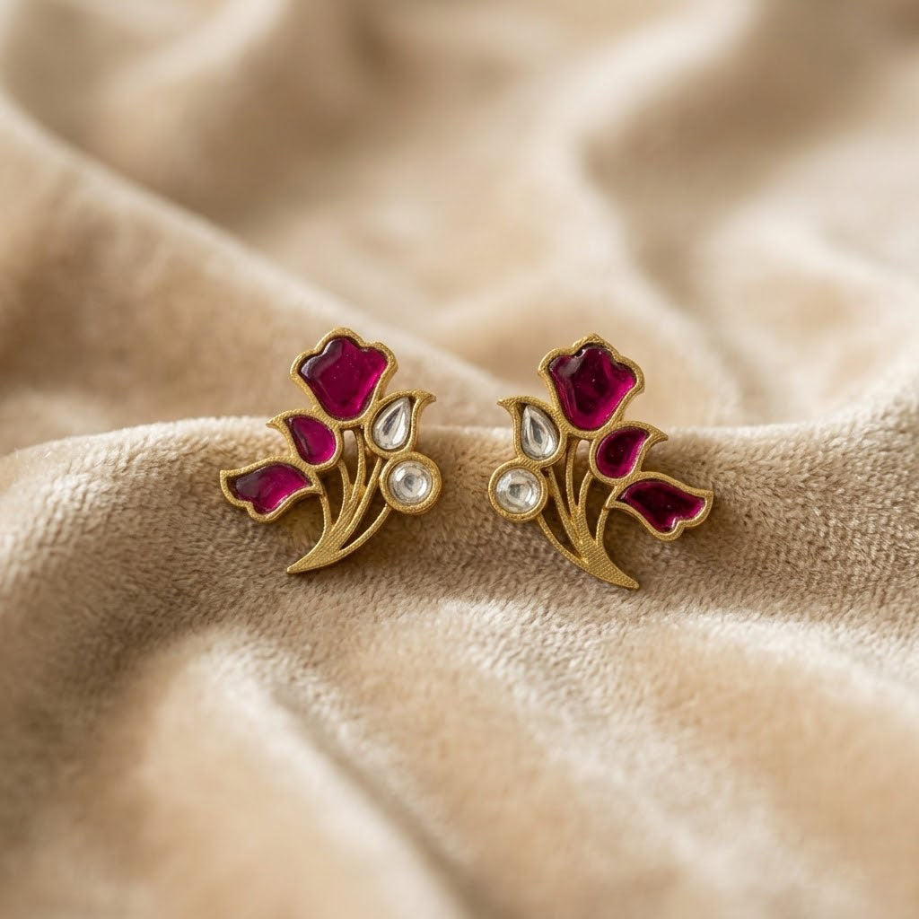 A pair of vintage-style gold floral stud earrings with deep pink enamel petals and clear teardrop-shaped stones, resting on a soft beige fabric background.